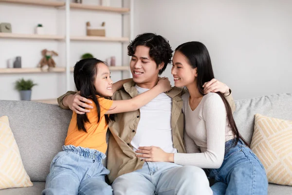 Positive pretty young japanese girl, mom and dad hugging on sofa have fun, enjoy tender moment — Fotografia de Stock