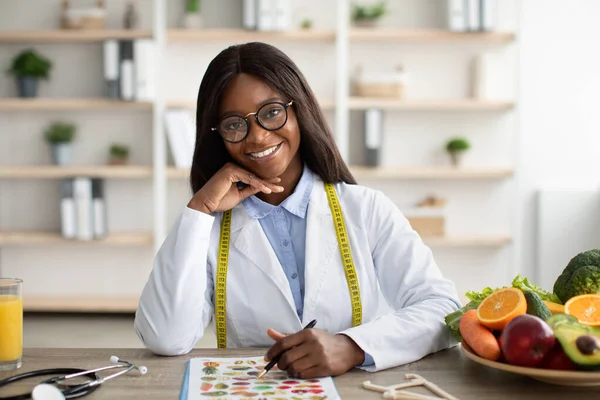 Portrait d'un heureux consultant afro-américain de perte de poids assis sur le lieu de travail et souriant à la caméra dans une clinique moderne — Photo