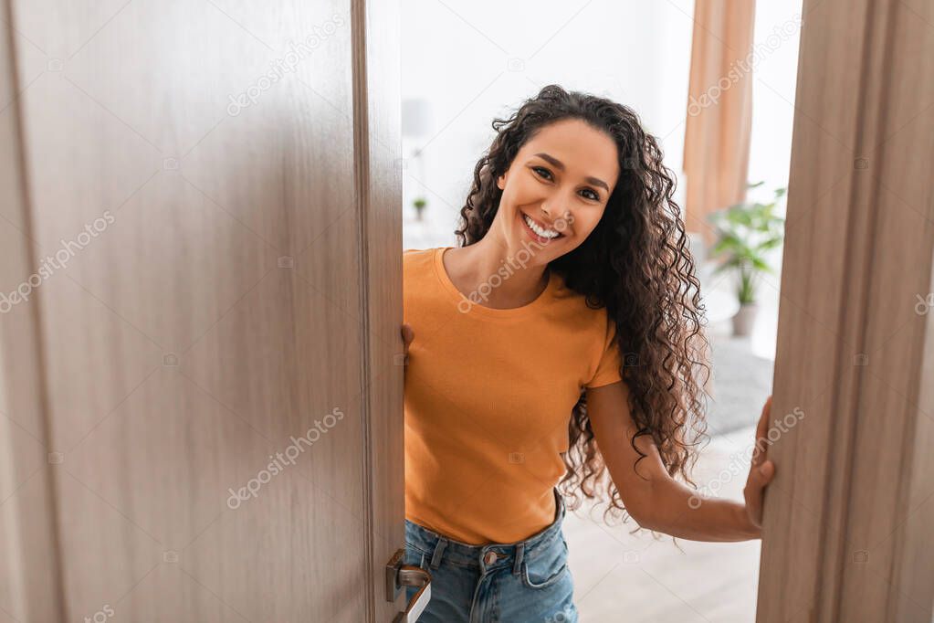 Cheerful young curly lady receiving guests at front door