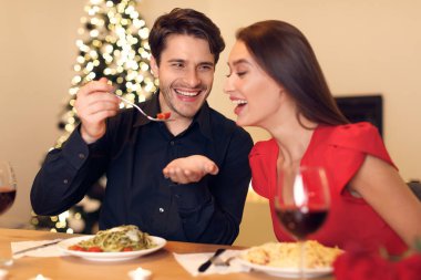 Smiling guy feeding his woman with pasta