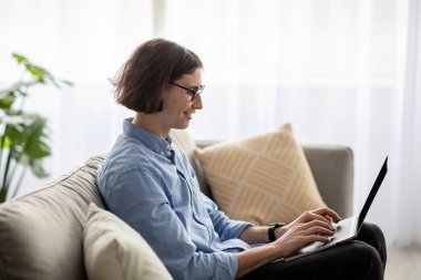 Handsome freelancer guy relaxing on sofa with laptop, enjoying domestic pastime and remote job opportunities, free space