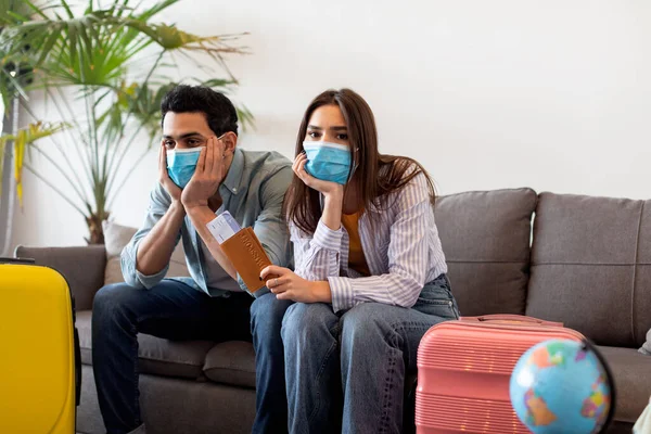 Cancelled flight. Upset spouses in medical face masks holding travel tickets, sitting with suitcases at home, copy space — Stock Photo, Image