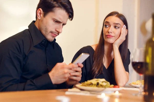 Mujer infeliz aburrido en la fecha, Hombre usando el teléfono —  Fotos de Stock