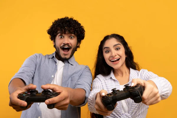 Concepto de estilo de vida. Feliz pareja india jugando videojuegos en línea, utilizando joystick gamepad, fondo amarillo —  Fotos de Stock