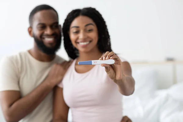Portrait of happy young african american man and lady show positive pregnancy test in bedroom interior, selective focus — Stock fotografie