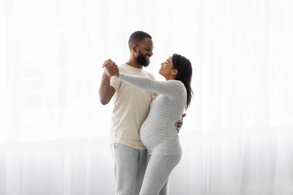 Satisfied cute young african american male and pregnant woman dance on window background, celebrate good news — Stock fotografie