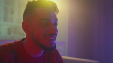 Young emotional carefree arab man playing video games or watching tv at home in evening, slow motion, free space