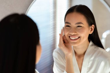 Cheerful pretty asian woman removing makeup with cotton pads