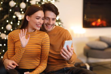 Smiling young couple using laptop at home, waving