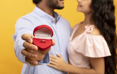 Marriage proposal concept. Loving indian couple hugging, man holding box with engagement ring, selective focus, closeup