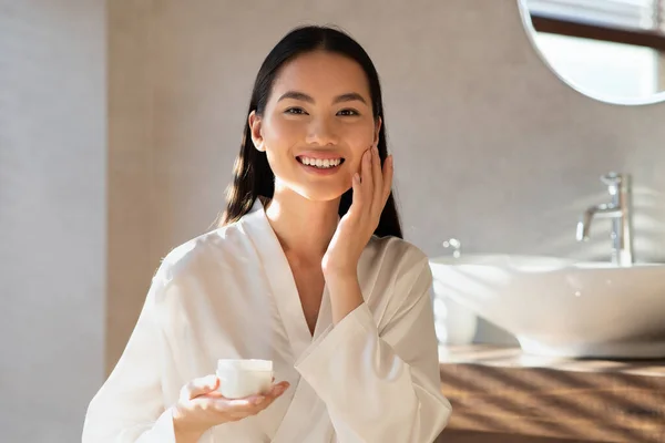 Молода красива азіатська дама використовує зволожуючий крем для обличчя — стокове фото