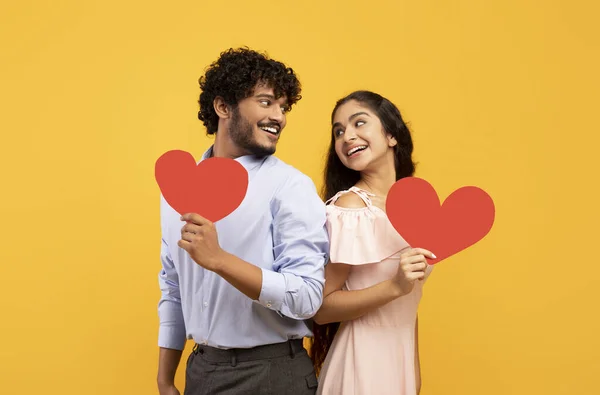 Día de San Valentín. Retrato de amantes indios sosteniendo corazones de papel rojo y mirándose el uno al otro, fondo amarillo — Foto de Stock