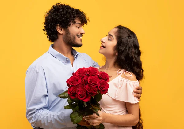 Lovers holiday. Loving indian couple holding bouquet of flowers, embracing, looking at each other on yellow background — Fotografia de Stock