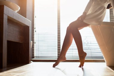 Unrecognizable lady in bathrobe sitting on bathtub