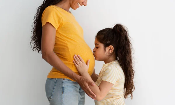 Expecting New Baby. Cute little girl kissing moms pregnant belly, side view — Stok fotoğraf