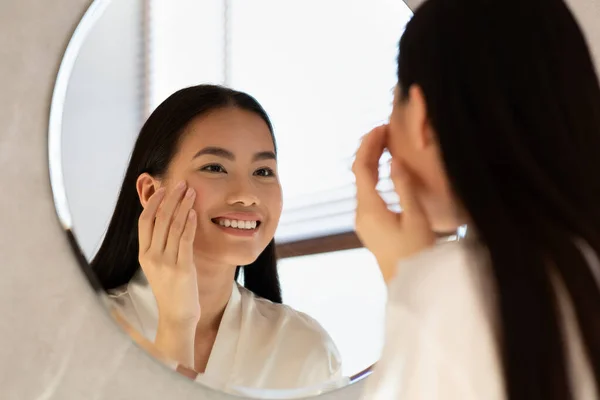 Mirror reflection of happy asian woman applying eye care product — Stok Foto