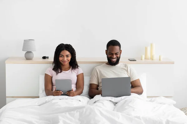 Smiling millennial african american guy with pc, lady with tablet surfing in internet, chatting in social networks — Stok Foto