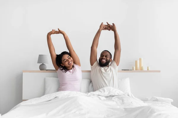 Smiling young african american male and female woke up stretching body and enjoy morning on comfort white bed — Stock Fotó