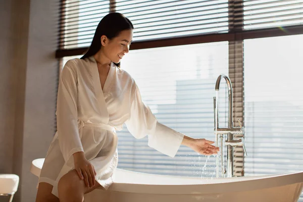 Vrolijke mooie koreaanse vrouw vullen bad met water — Stockfoto