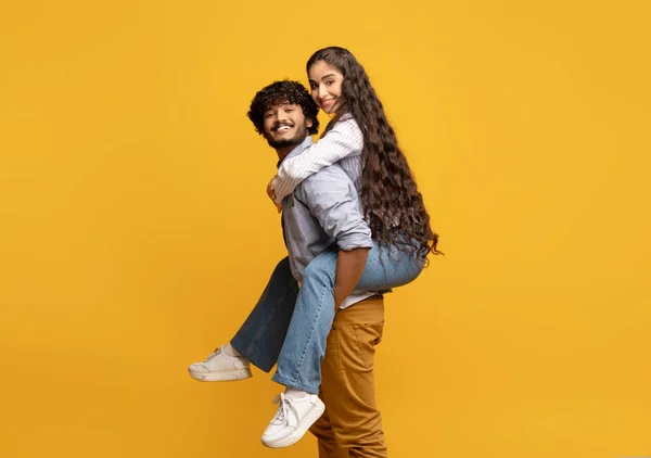 Νεαρός Ινδός που κάνει βόλτα με το γουρουνάκι στην κοπέλα του σε κίτρινο φόντο στούντιο, ελεύθερος χώρος — Φωτογραφία Αρχείου