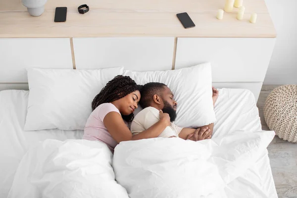 Calm cute peaceful young african american woman hugs man and sleeps on comfort bed together in bedroom, profile — Stok fotoğraf