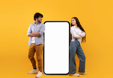 Mobile offer. Millennial indian couple leaning on giant smartphone with mockup, promoting app or website
