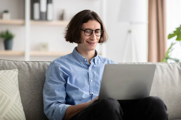 Distant work. Happy young freelancer man using laptop computer, working remotely frm home, sitting on sofa — Stock Photo, Image