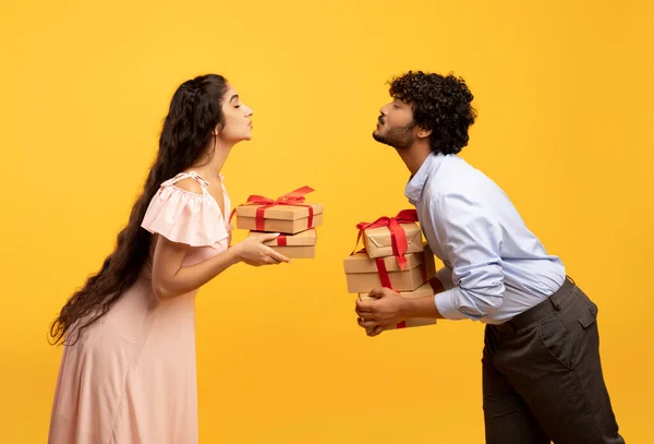 Романтические индийские любовники обмениваются подарками на День Святого Валентина или годовщину, пытаясь поцеловать друг друга, вид сбоку — стоковое фото