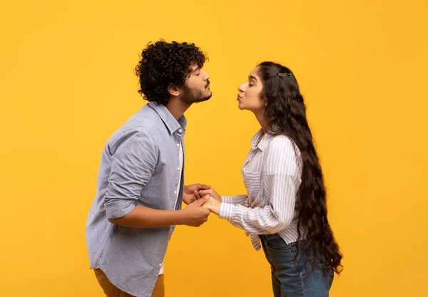 Young indian couple reaching each other with lips, ready to kiss over yellow background, side view — Φωτογραφία Αρχείου