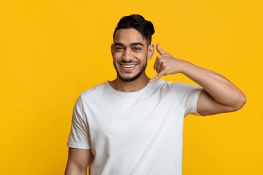 Cheerful middle eastern young man showing call me gesture
