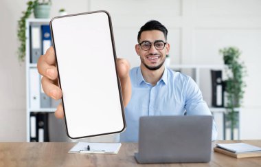 Mobil anlaşma. Arap İşadamı Ofiste Otururken Büyük Boş Akıllı Telefonu Gösteriyor