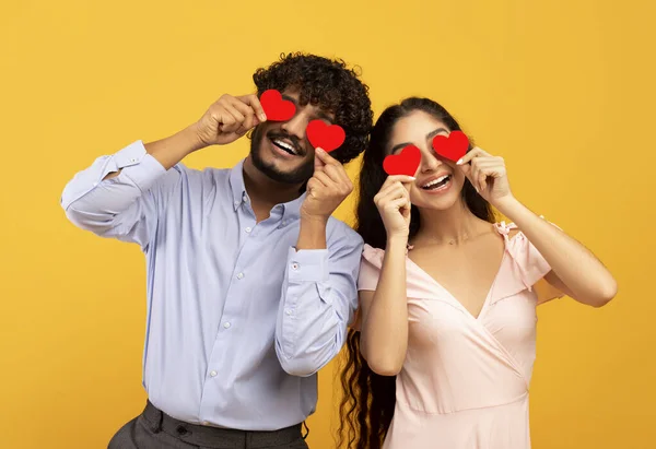 Amantes cegados por su gran amor. Joven pareja india enamorada sosteniendo tarjetas rojas en forma de corazón sobre los ojos — Foto de Stock