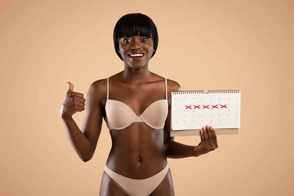 CHeerful fekete nő fehérneműben naptárral mutatja hüvelykujját felfelé — Stock Fotó