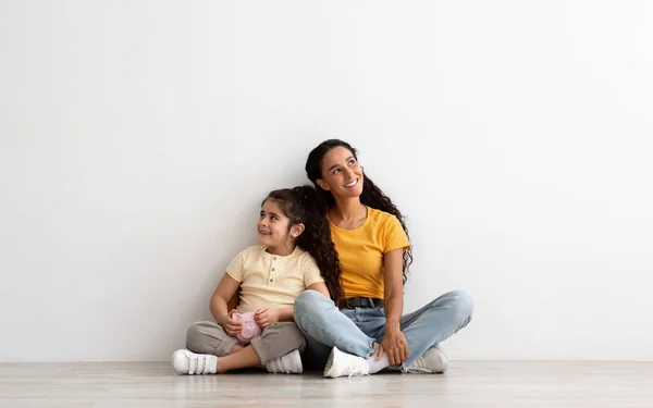 Inversión familiar. Soñadora madre e hija sosteniendo alcancía y mirando hacia otro lado — Foto de Stock
