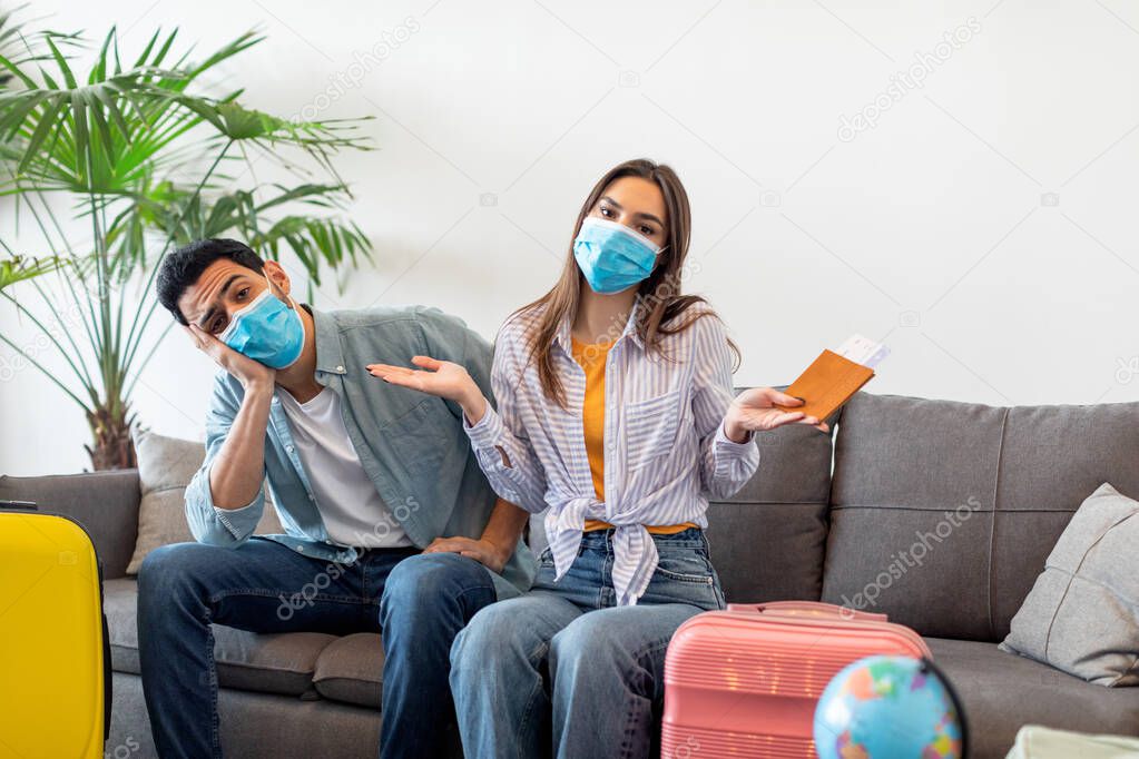Upset tourists couple after tour cancellation sitting on sofa with paked suitcases and travel tickets