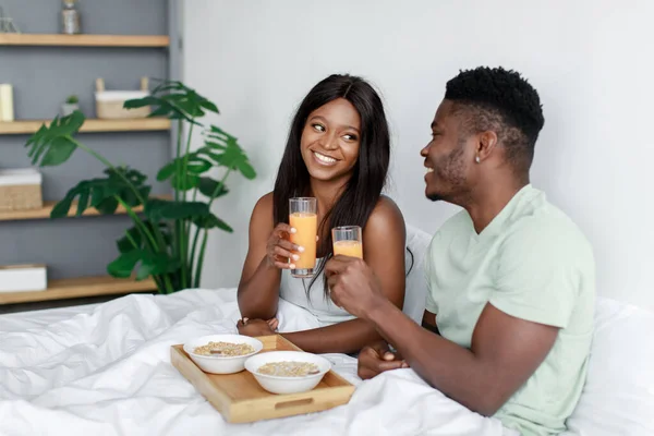 Happy pretty young african american woman and man woke up after night sleep on bed in bedroom have healthy breakfast — Foto de Stock