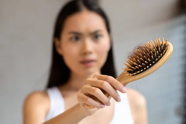 Preocupado millennial ásia mulher segurando escova de cabelo, close-up — Fotografia de Stock