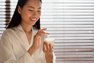 Smiling chinese woman holding jar with beauty product