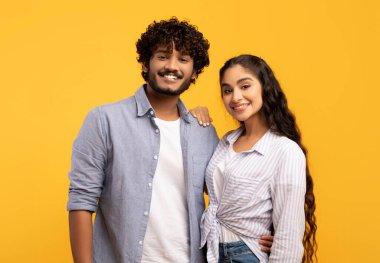 Romantic couple. Portrait of happy indian man and woman embracing and smiling at camera on yellow background