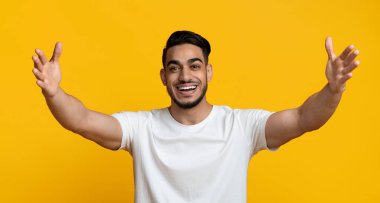 Charismatic young arabic guy outstretching hands on yellow