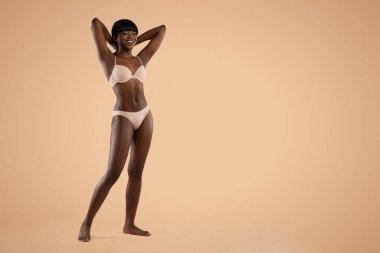 Happy attractive black lady posing in underwear on beige
