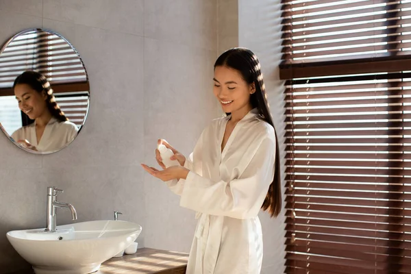 Atractiva mujer asiática de pelo largo sosteniendo botella con producto de belleza — Foto de Stock