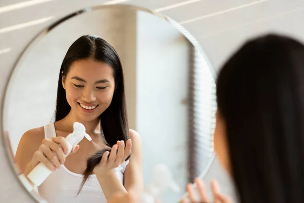 Senyum wanita muda asia berambut panjang menggunakan hair spray — Stok Foto