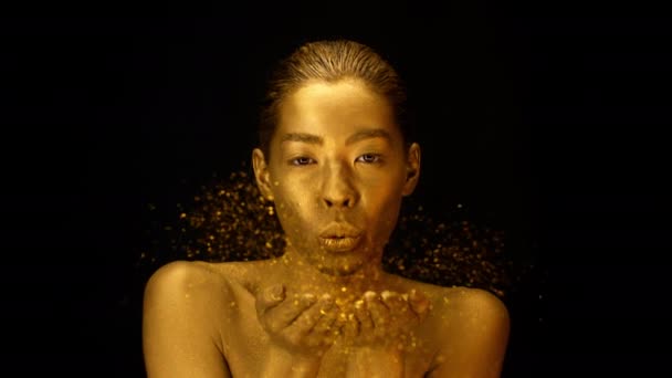 Female With Golden Skin Blowing Gold Dust Over Black Background — Stok video