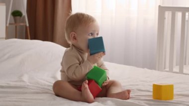 Adorable Infant Baby Sitting In Bed And Playing With Stacking Building Blocks