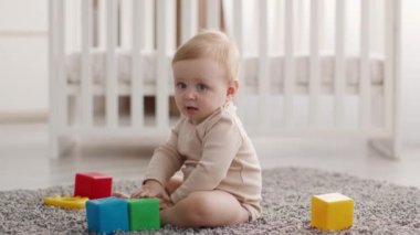 Cute Infant Baby Boy Sitting On Floor And Playing With Building Blocks
