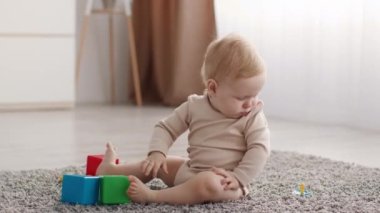Cute Baby Playing With Pacifier While Sitting On Floor In Living Room
