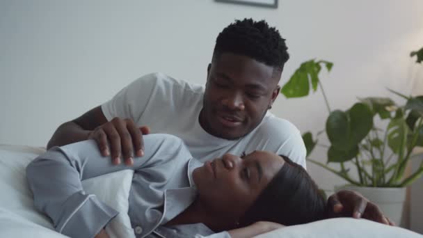 Guten Morgen, Schatz. Junge liebevolle afrikanisch-amerikanische Mann weckt seine schöne Frau, liegen und reden zusammen im Bett — Stockvideo
