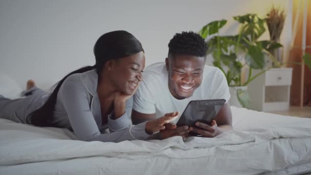 Memórias felizes. Jovem casal afro-americano recém-casados descansando na cama e assistindo fotos em tablet digital de manhã — Vídeo de Stock