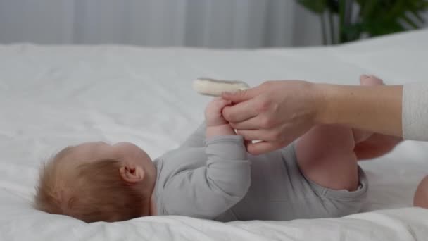 Неузнаваемая мать, играющая с милым пухлым ребенком, лежащим дома на кровати — стоковое видео